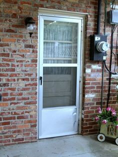 a brick wall with a white door and window next to a potted planter