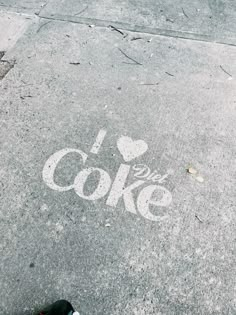 someone's feet are standing on the sidewalk next to a painted i love coke sign