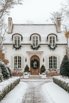 a house covered in snow with wreaths on the front door and entry way leading to it