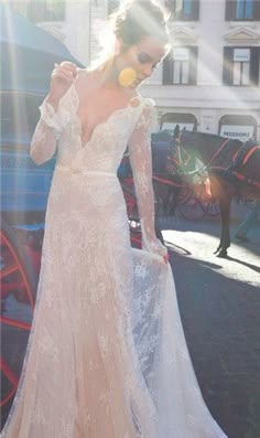 a woman in a white wedding dress standing on the street with a horse drawn carriage behind her