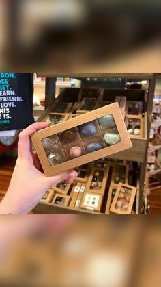 a person holding up a box of chocolates in front of a store display case