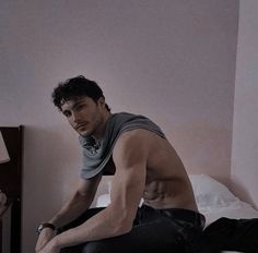 a shirtless man sitting on top of a bed