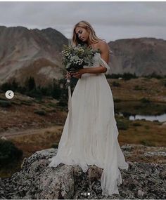 a woman standing on top of a mountain holding a bouquet