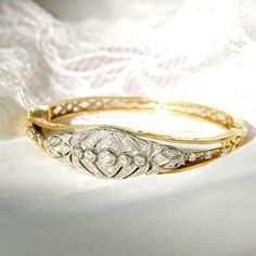 An astounding Edwardian era diamond cluster hinge bangle bracelet in 14k yellow gold and platinum. Features an ornate diamond-encrusted platinum navette setting mounted on a tapered gold band with cutout embellishments and a latch box clasp. Built into the focal point of this bracelet is 5 round-cut diamonds secured in a horizontal line of bezel settings. The open work on either side of the platinum setting is also decorated with three prong-set diamond accents. All the diamonds seem to be in go Native Jewelry, Luxury Rings, Box Clasp, Ring Pendant Necklace, Edwardian Era, Hinged Bangle, May 2023, Diamond Cluster, Gold Band