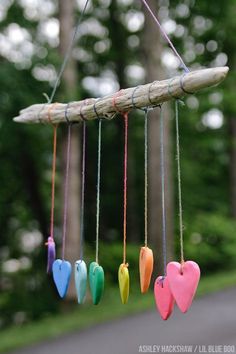 colorful hearts hanging from a tree branch in the wind with string attached to it and some wood sticks sticking out of them