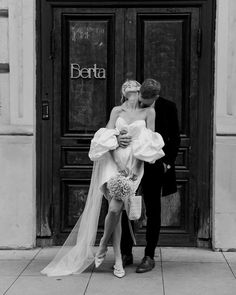 a bride and groom kissing in front of a building with the name berta written on it