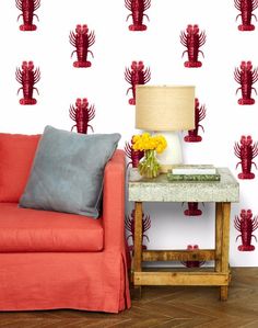 a red couch sitting next to a table with a lamp on it in front of a wall