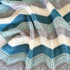 a crocheted blanket is laying on top of a white table with blue and gray stripes