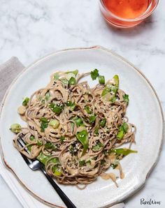 a white plate topped with noodles and veggies next to a cup of tea