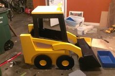 a yellow toy bulldozer sitting on top of a floor next to a trash can