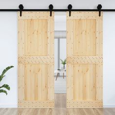 an open wooden door with black hardware on the top and bottom, in front of a white wall