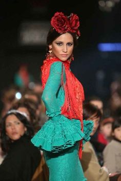 a woman is walking down the runway wearing a green dress with red flowers in her hair