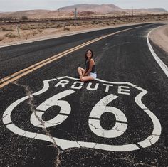 a woman sitting in the middle of an empty road with route 66 painted on it