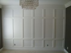 an empty room with white paneling and a chandelier