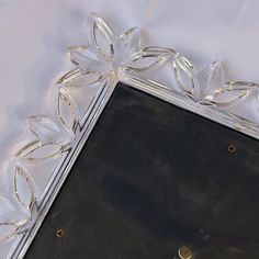 a silver and glass frame with flowers on it's edge, sitting on a white table cloth