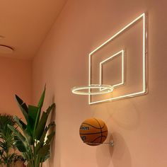 a basketball is hanging on the wall next to a plant and neon hoop in a room with pink walls