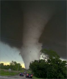 a large tornado is seen in the sky above two cars