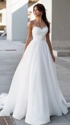 a woman in a white wedding dress standing on the sidewalk