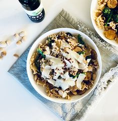 two bowls filled with pasta, broccoli and other food items on a table