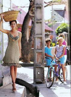 a woman standing next to a bike with a basket on it's head and two other women walking behind her