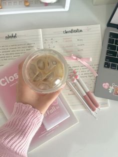 a person's hand holding onto a cup filled with liquid next to a laptop