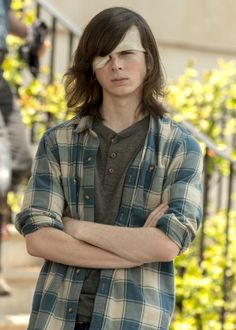 a young man with his arms crossed standing in front of some bushes and stairs,