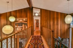 a hallway with wood paneling and hanging lamps on the wall, along with an area rug