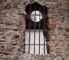 the moon is seen through a barred window in an old stone building with iron bars