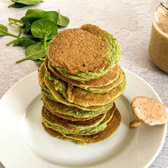 a stack of green pancakes sitting on top of a white plate next to a jar of peanut butter