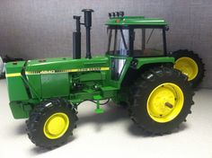 a green and yellow toy tractor sitting on top of a white table next to a gray wall