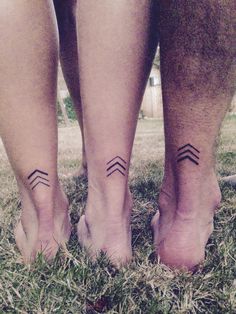 two people with matching tattoos on their feet standing in the grass and holding hands together