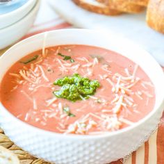 there is a bowl of soup with cheese and broccoli on the table next to bread