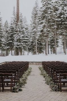 an outdoor ceremony setup with rows of chairs and greenery on the aisle, surrounded by snow covered pine trees