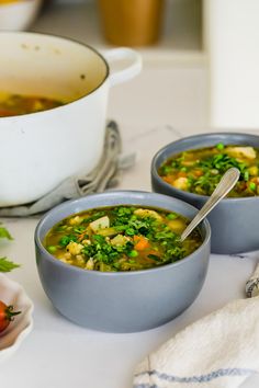 two bowls filled with soup next to a bowl of tomatoes and parsley on the side