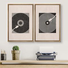 two framed art prints on the wall above a desk with an old typewriter and record player