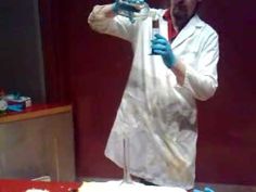 a man in white lab coat and blue gloves standing next to a cake with frosting on it