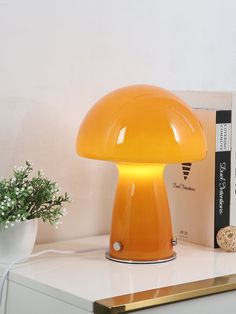 an orange mushroom shaped lamp sitting on top of a white table next to a plant