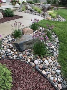 a garden with rocks and flowers in the front yard, along with landscaping plants on either side