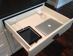 an open drawer with a laptop, tablet and charger in it on the counter