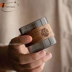 a person holding a wooden cup in their hand with the lid up to show it's logo