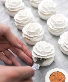 someone is spreading icing on some cupcakes with white frosting and rose decorations