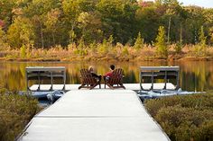 two people sitting on chairs at the end of a dock