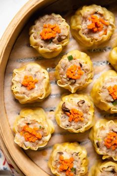 a wooden bowl filled with dumplings covered in cheese and carrots