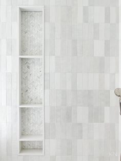 a white tiled bathroom with a shelf above it