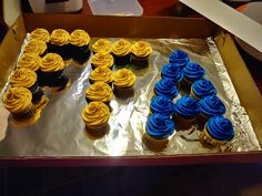 a box filled with lots of cupcakes on top of tin foil covered in blue frosting