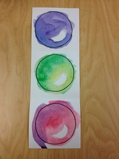 three circles painted in different colors on a piece of paper next to a wooden table