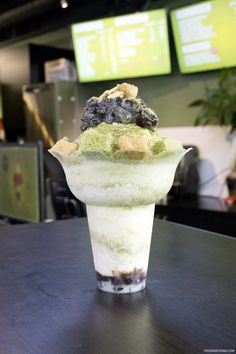 an ice cream sundae with blueberries and green toppings on top sits on a table