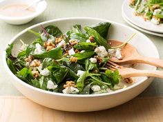 a salad with spinach, feta cheese and walnuts in a white bowl