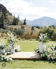 an outdoor ceremony setup with white flowers and greenery on the ground in front of mountains