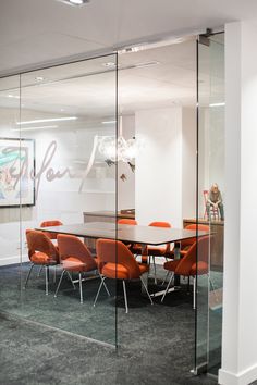 an office meeting room with glass walls and orange chairs